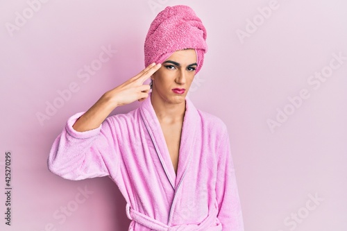 Young man wearing woman make up wearing shower towel on head and bathrobe shooting and killing oneself pointing hand and fingers to head like gun, suicide gesture.