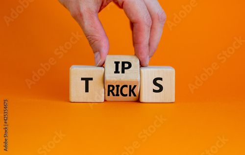 Tips and tricks symbol. Businessman turn the wooden cube and changes the word 'tips' on 'tricks'. Beautiful orange background. Business and tips and tricks concept, copy space.