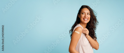 Woman Showing Vaccinated Arm With Bandage After Injection, Blue Background