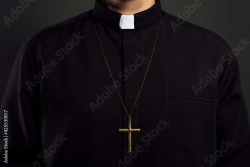 Priest with cross on black background, closeup
