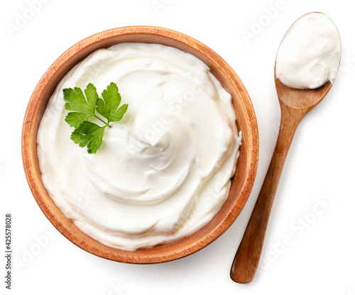 Sour cream in a wooden plate and spoon on a white background, isolated. The view from top