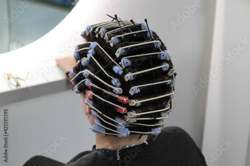 young woman with hair curlers on head, getting perm from hairdresser