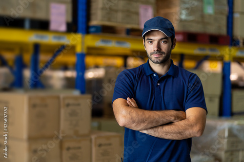Confident male warehouse worker standing with arms crossed in factory warehouse near of products or parcel goods background. Inspection quality control