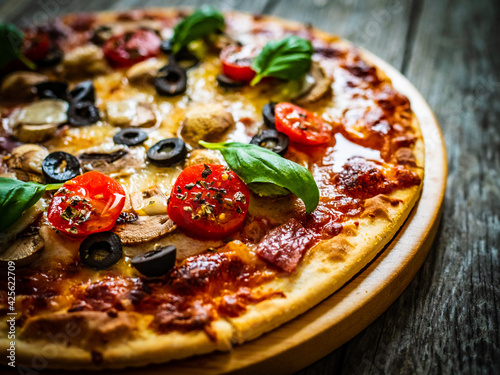 Pizza with white mushrooms, ham, tomatoes, olives, parmesan and mozzarella on wooden background 