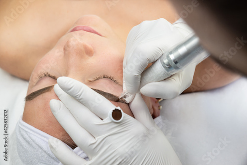 Konturowanie brwi, proces pigmentacji brwi. Kobieta w salonie urody w trakcie zabiegu, makijaż permanentny. 