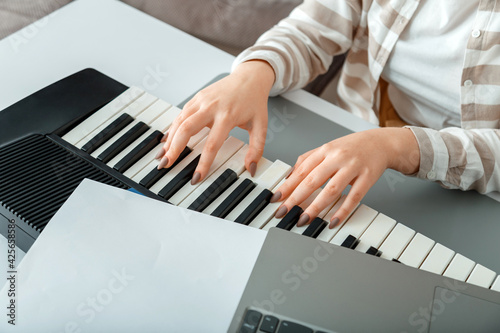 Woman playing piano record music on synthesizer using notes and laptop. Female hands musician pianist improves skills playing piano. Online Music education hobby vocals singing using piano.