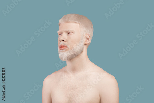 Albinism concept. Thin albino man posing without shirt and lookig aside on turquoise studio background