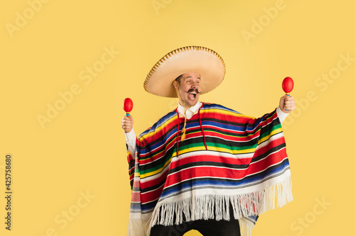 Happy man in sombrero and bright poncho isolated over yellow background