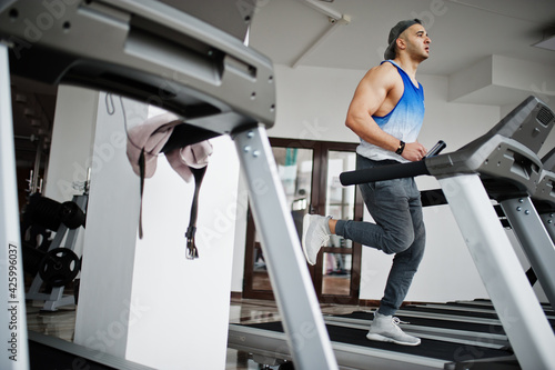 Fit and muscular arabian man running on treadmill in gym.