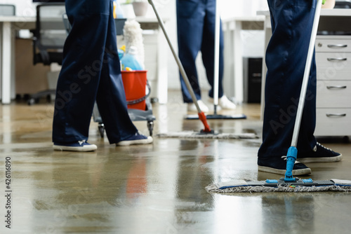 Cropped view of cleaners washing floor with mops in office
