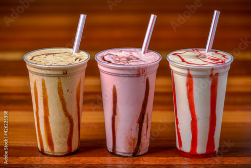 Milk shakes in plastic cups and straws on a dark wooden table.