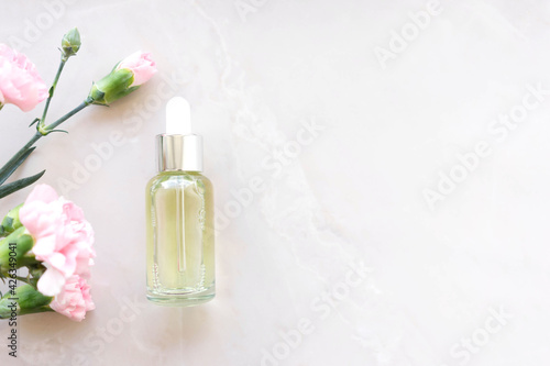 face serum on light background with pink flowers. Sensitive skin care concept. Copy space