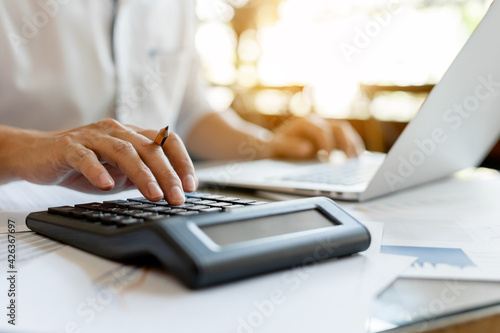 Close up businessman pressing on calculator for calculating cost estimating with laptop.