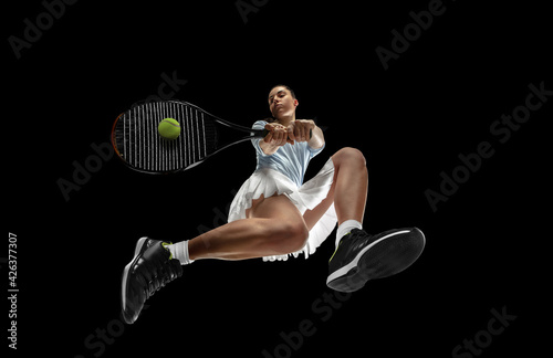 Female professional tennis player in action, motion isolated on black background, look from the bottom. Concept of sport, movement, energy and dynamic.