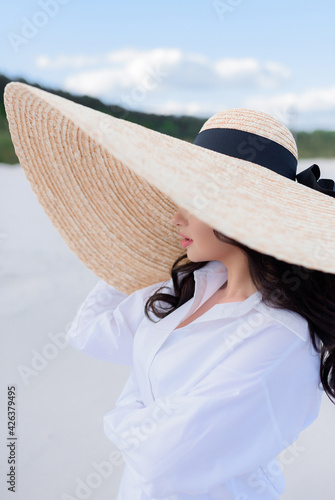 Close up of young brunette with a big hat stands on the sand. Сoncept of recreation on the beach