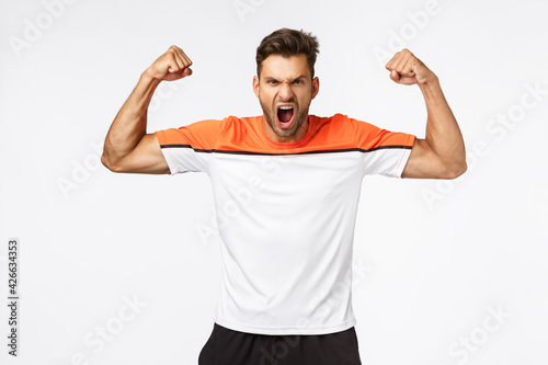 Power, sport and fitness concept. Handsome strong and powerful aggressive man brag perfect shape, shouting, encourage gym visitors train hard, showing muscles, standing white background