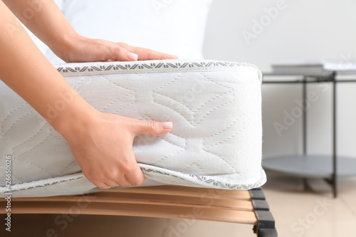 Woman putting soft orthopedic mattress on bed, closeup