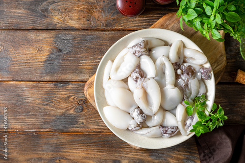 Raw cuttlefish in a ceramic plate on the kitchen table. Lots of peeled squid in a bowl on a brown wooden table top view. The concept of cooking shellfish