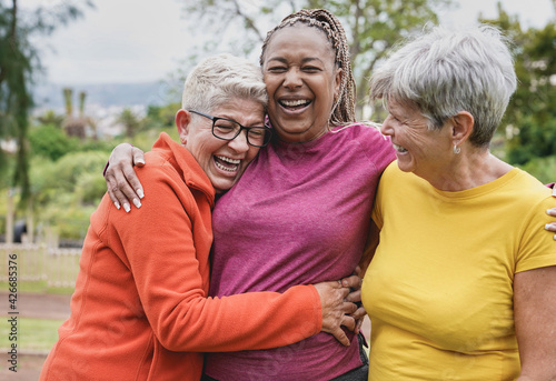 Happy multiracial senior women having fun together at park - Elderly generation people hugging each other outdoor