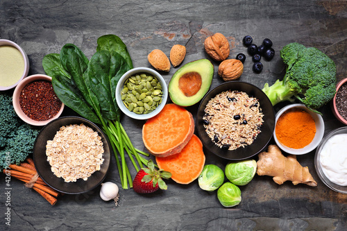 Selection of healthy food ingredients. Overhead view table scene on a dark slate background. Super food concept with green vegetables, berries, whole grains, seeds, spices and nutritious items.