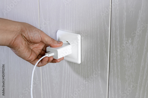 Hand turns on, turns off charger in electrical outlet on wall