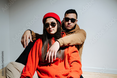 Stylish cool looking young couple in sunglasses and hoodies sitting on the floor