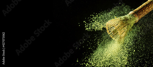 Bamboo whisk with flying matcha tea powder on black background with copy space.