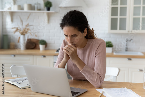 Hard to decide. Anxious worried latin woman freelancer sit at kitchen workplace meet difficult problem mistake ponder on decision. Scared young lady think by laptop screen troubled with debt blackmail