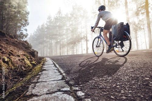 Cyclist on a bicycle with panniers riding along a foggy forest road