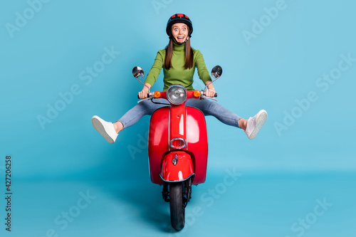 Full size portrait of funny carefree lady driving bike raise legs open mouth isolated on blue color background