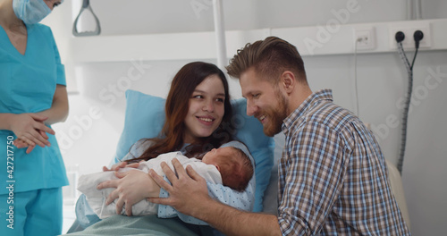 Young couple with doctor holding newborn baby in hospital ward