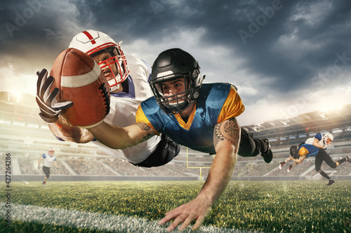 American football players in fight for goal at stadium in flashlights. Professional sportsman during game playing in action and motion.