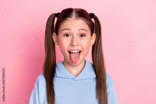 Photo portrait of funky schoolgirl showing tongue fooling playful isolated on pastel pink color background