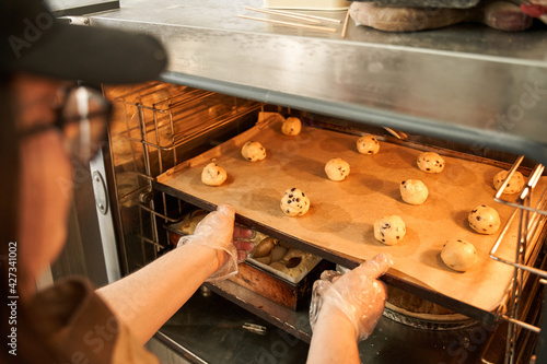Baker putting tray with balls from the dough to the oven while making cookies