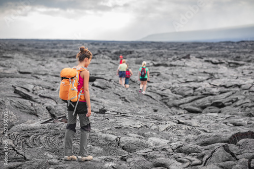 Hiking group of hikers walking on Hawaii volcano lava field hike adventure happy woman with backpack in Big Island, Hawaii. Tourists walking on guided tour trail outdoor USA summer travel vacation.