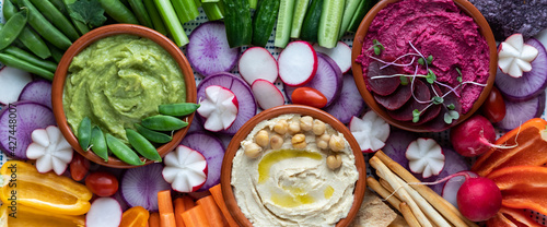 Narrow close up view of three dips surrounded by fresh cut vegetables for dipping.