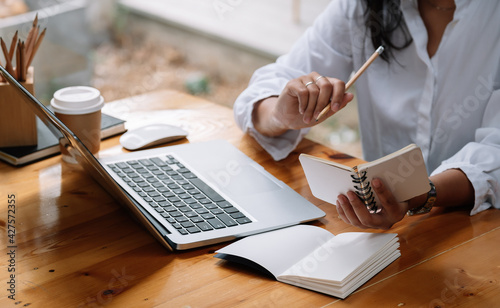 Cropped photo of woman writing making list taking notes in notepad working or learning on laptop indoors- educational course or training, seminar, education online concept.