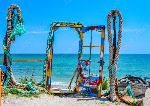 Landscape photo of colorful instalation on the beach, colored ropes and a door leading towards the Black Sea during a sunny summer day with blue sky and water waves at Vama Veche, Romania
