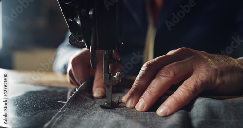 Macro shot of experienced tailor is sewing custom handmade high quality apparel in ancient luxury traditional tailoring workshop. Concept of industry, handmade, hand craft, couturier and tradition.