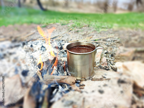 Metal cup of tea or coffee on bonfire, camping atmosphere background