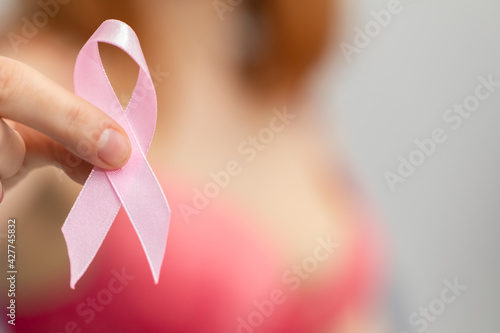 A woman holds a pink ribbon in her hand - Symbol of the fight against breast cancer.