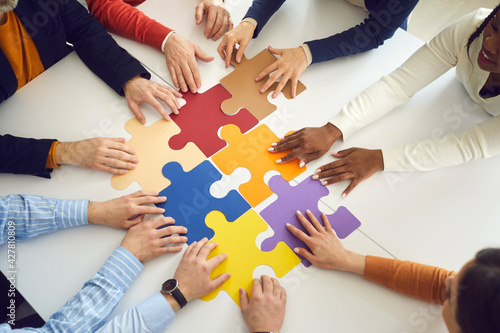 Solidarity, strategy collaboration, business workflow and communication research concept. Diverse multiethnic office people team assembling jigsaw puzzle pieces holding hands on table top view