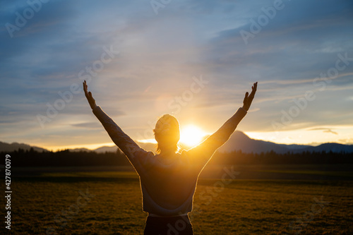 Woman embracing life standing outside in beautiful meadow with her arms raised high