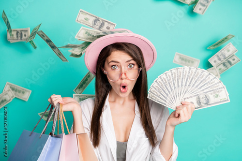 Photo of sweet excited young woman dressed white shirt cap glasses shopping holding money isolated teal color background