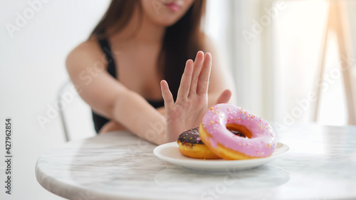 Close up female hand pushing out avoid say no her favorite donut sweets for good health and weight control as diet and healthy concept