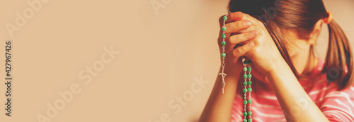 Young girl holding rosary and praying to God.