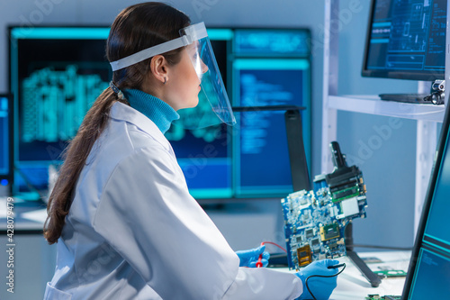 Female microelectronics engineer works in a scientific laboratory on computing systems and microprocessors. Professional electronic factory worker is testing the motherboard and coding the firmware.