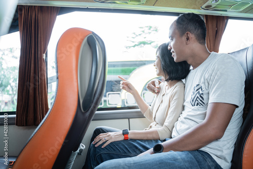 a young man and a young woman finger pointing at the window while sitting on the bus while traveling