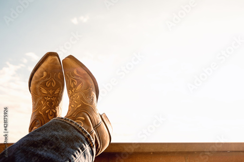 cowboy resting legs with feet crossed - sky background - negative space - boots and jeans