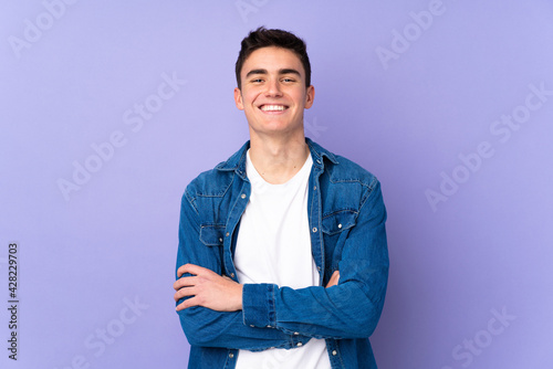 Teenager caucasian handsome man isolated on purple background keeping the arms crossed in frontal position